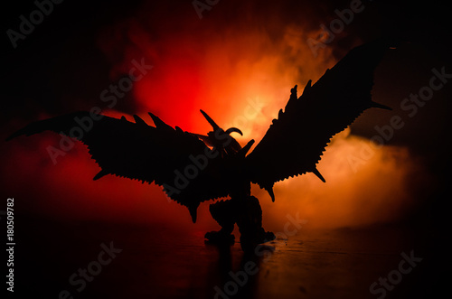 Silhouette of fire breathing dragon with big wings on a dark orange background. Empty space