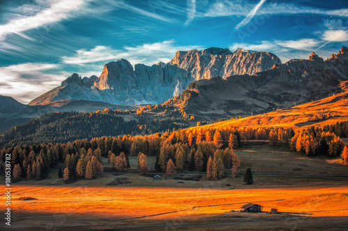 Aerial autumn sunrise scenery with yellow larches and small alpine building and Odle - Geisler mountain group on background. Alpe di Siusi (Seiser Alm), Dolomite Alps, Italy
