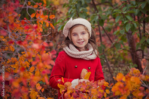 Cute young russian girl stylish dressed in warm red handmade jacket blue jeans boots and hooked headband scarf posing in autumn colorful forest pathway Face with freckling