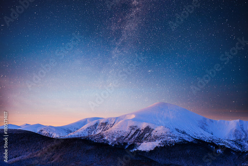 Beautiful winter landscape in the Carpathian mountains. Vibrant night sky with stars and nebula and galaxy. Deep sky astrophoto