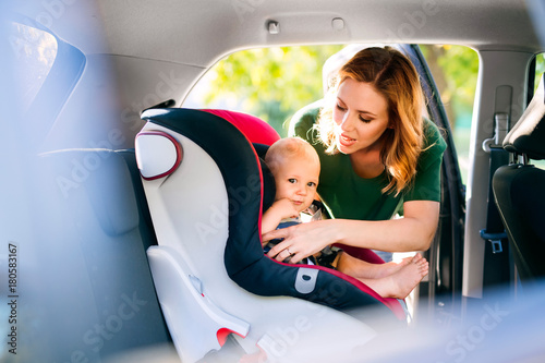 Young mother putting baby boy in the car seat.