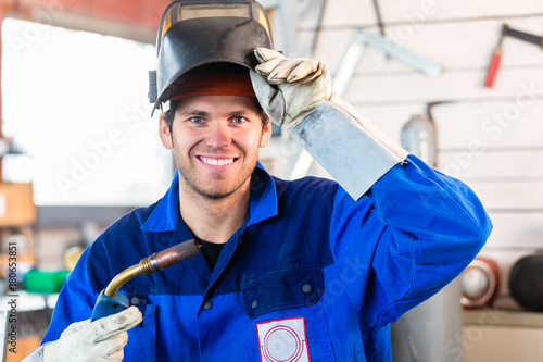 Welder with welding device in metal workshop looking into camera