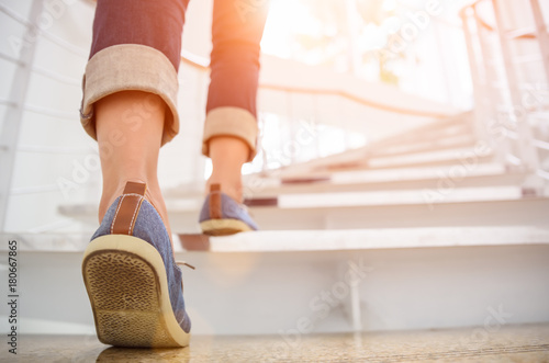 Young adult woman walking up the stairs with sun sport background.