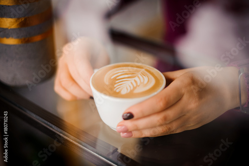 Female hands holding a cup of coffee latte with art outside the window
