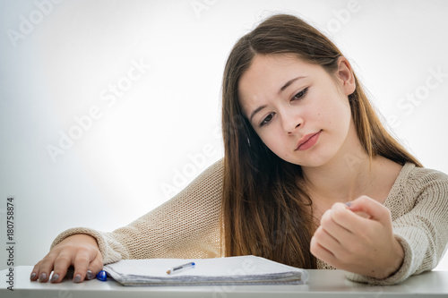 Bored teenager girl checking her nails instead of studying