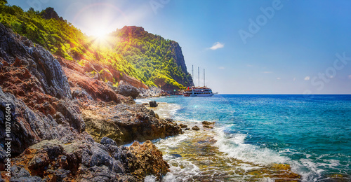 Tropical rocky beach on sunny summer day in Alanya, Turkey. Sea and mountains landscape with waves. Lagoon bay. Panoramic view on paradise coastline. Summer vacation nature. Adventure and travel.