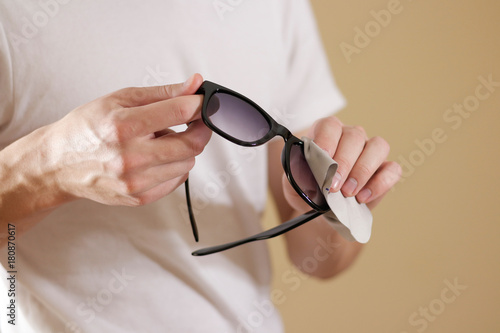 Man in white t shirt hand cleaning black sun glasses lens with isolated background