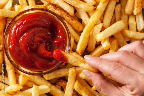 Hand dipping french fries in tomato sauce or ketchup