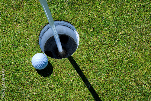 Close up of golf green with ball next to the hole, with the flag pole in 
