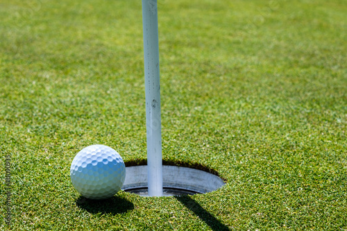 Side view of a golf green with the golf ball on the edge of the hole, with the flag pole in 