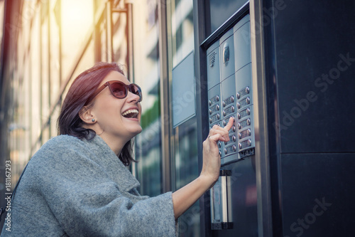 Happy woman using intercom at building entrance.