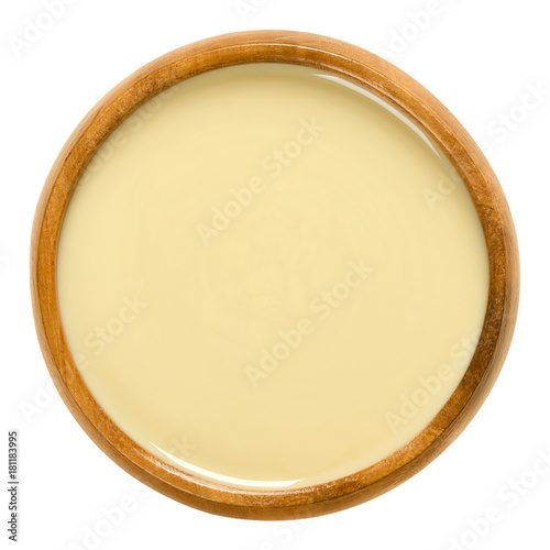 White almond butter in wooden bowl. Smooth food paste made of shelled blanched almonds. Fine puree of the nuts of Prunus dulcis. Isolated macro food photo close up from above on white background.