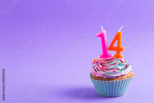 Festive creamy cupcake with sprinkles and candles in the form of number 14 on purple background