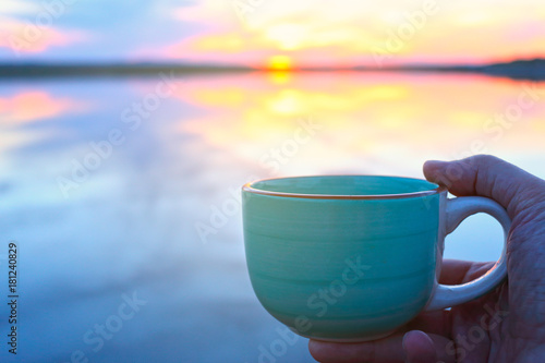 Cup coffee in hand on the beautiful summer sunset background 