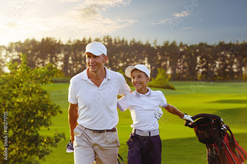 Happy man with his son golfers walking on perfect golf course at summer evening