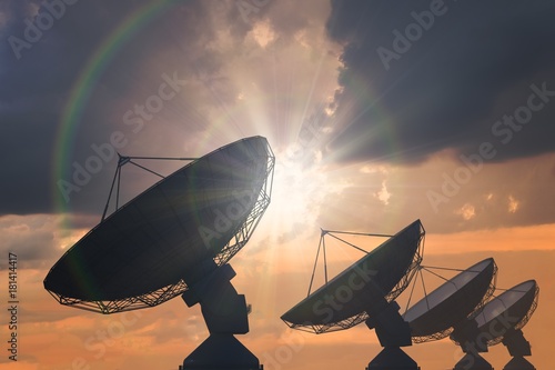Silhouettes of array of satellite dishes or radio antennas at sunset.