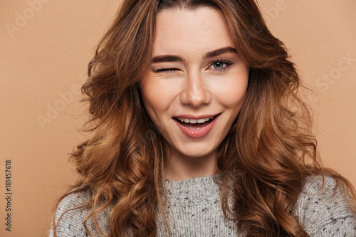 Close-up photo of young charming brunette woman blinks one eye and looking at camera