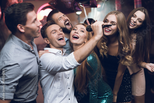 Young people in the club dance and sing. A man in a white shirt is holding a microphone and singing.