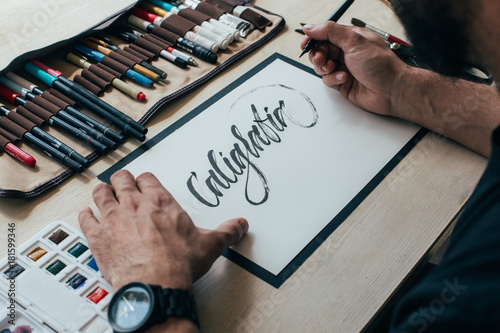 View on big sheet of white paper canvas with word calligraphy spelled on top using brush with black ink by font designer or creative artist freelancer working on project in home studio