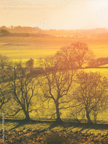 Red, Orange and yellow glow of a sunset over green pastures and trees in the English Countryside.
