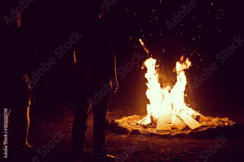 Camping vacation outdoors, bonfire in the night, bright with sparkles and people silhouettes