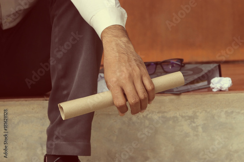 Close up hand of businessman holding Resignation document and sits on the stairs down in his work. Stressed and Unsuccessful concept. Use for background and banner. Vintage Tone.