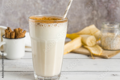 Banana oat protein shake with cinnamon and paper straw in a glass.