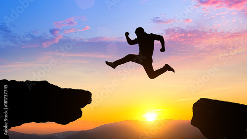Man jumping over cliff on sunset background