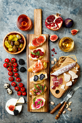 Appetizers table with italian antipasti snacks and wine in glasses. Brushetta or authentic traditional spanish tapas set, cheese variety board over grey concrete background. Top view, flat lay