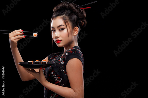 Asian woman with sushi eating sushi and rolls on a black background.