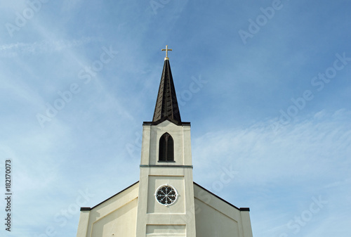 Christian background photo of a majestic church steeple with a cross and a clock tower on a blue sky background