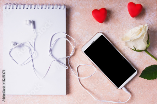 Notepad, smartphone with headphones, white rose and hearts, copy space - Mock up Valentine's Day