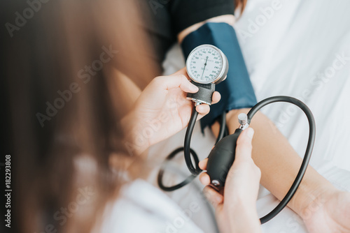 Back view of doctor checking blood pressure of a patient with sphygmomanometer in bed