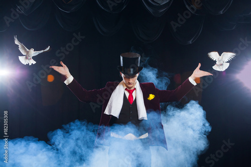 The magician with a two flying white Doves. on a black background shrouded in a beautiful mysterious smoke