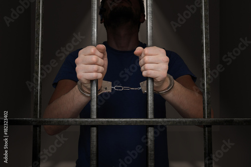 Arrested prisoner is holding bars in prison cell.