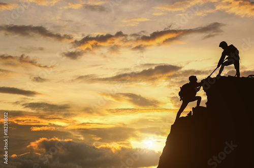 Male and female hikers climbing up mountain cliff and one of them giving helping hand.