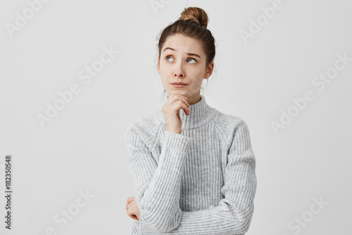 Young woman with dark hair holding her chin looking sideways. Attractive girl having meaningful gaze to side thinking about her future wistfully. Life goals concept