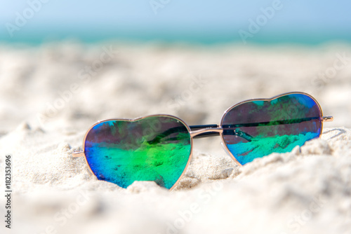 Summer Fashion heat shape sunglasses on sea beach under clear blue sky. Summer holiday relax background with copy space.