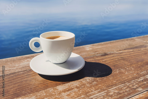 Cup of coffee on a table over sea background. Summer holiday concept