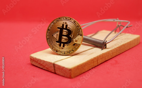 Mousetrap with gold bitcoin on red background.