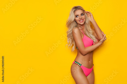 Smiling Sexy Blond Woman In Pink Bikini Is Looking Over The Shoulder At Copy Space