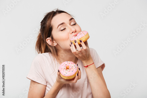 Close up portrait of a satisfied pretty girl eating donuts