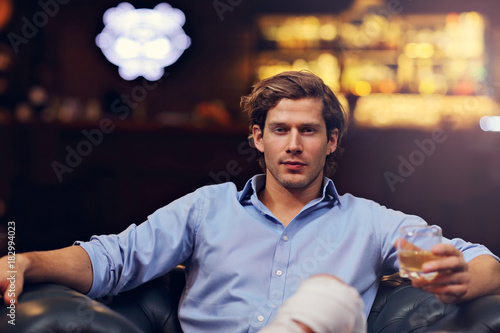 Young man sitting alone in bar with a glass of whisky