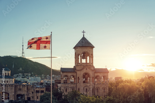 View of the sunset of the bell tower in Tbilisi, Georgia. And the flag of Georgia developing in the wind.