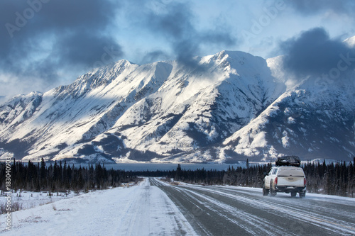 A car driving towards mountains on the Alaska Highway