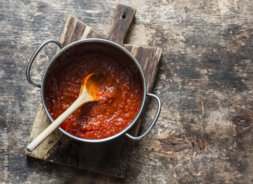 Classic homemade tomato sauce in the pan on a wooden chopping board on brown background, top view. Pasta, pizza tomato sauce. Vegetarian food