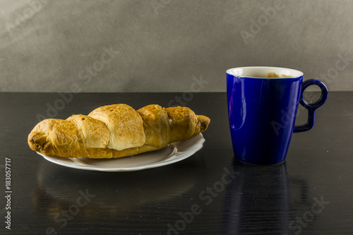 Gold croissant and a cup of coffee for breakfast.