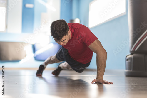 Jove hombre entrena flexiones a una mano en el suelo del gimnasio