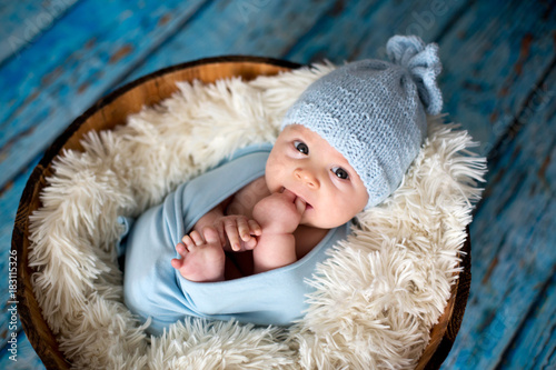 Little baby boy with knitted hat in a basket, happily smiling