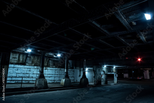 Dark Chicago city street with an industrial urban train bridge underpass at night.